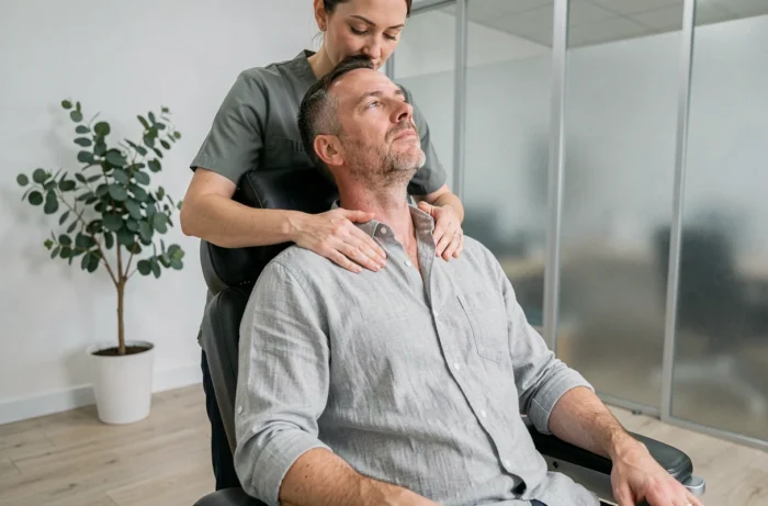 Homme d'âge mûr recevant un massage des épaules et du cou en position assise dans un studio bien-être moderne, thérapeute professionnel en action